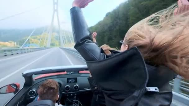 2 つの美しい若い女の子は、山の中で赤いカブリオレに乗る。高速道路の道。黒革のジャケットに身を包んだ。風になびく髪。旅行と自由をお楽しみください。. — ストック動画