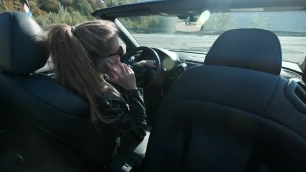 Ein junges Mädchen, das mit einem Smartphone spricht. sitzt in einem Cabrio in der Nähe hoher Berge. — Stockvideo