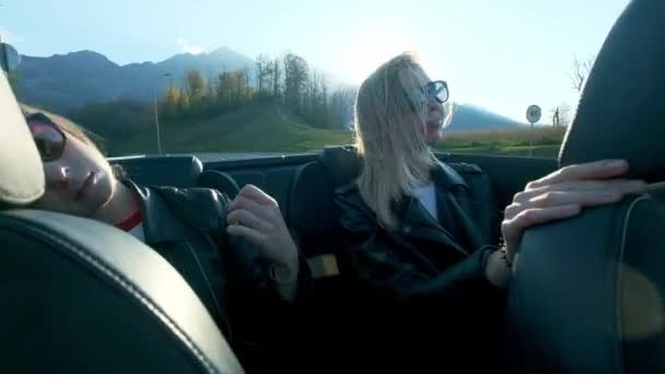 Deux jeunes belles filles en lunettes noires et vestes en cuir roulent dans un cabriolet rouge près des hautes montagnes. La vie est gouvernée, obtenir la liberté . — Video