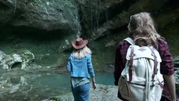 Dos jóvenes viajeras caucásicas viajan a lo largo de una cueva tropical. En la mochila trasera marchando. Inspirado en la belleza de la naturaleza. Buscando aventura en lugares exóticos del planeta. Estilo de vida activo . — Vídeos de Stock