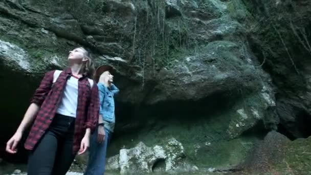 Dos jóvenes viajeras caucásicas viajan a lo largo de una cueva tropical. En la mochila trasera marchando. Inspirado en la belleza de la naturaleza. Buscando aventura en lugares exóticos del planeta. Estilo de vida activo . — Vídeos de Stock