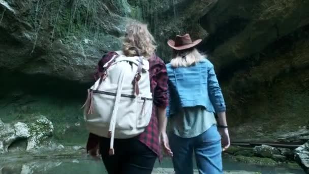 Dos jóvenes viajeras caucásicas viajan a lo largo de una cueva tropical. En la mochila trasera marchando. Inspirado en la belleza de la naturaleza. Buscando aventura en lugares exóticos del planeta. Estilo de vida activo . — Vídeos de Stock