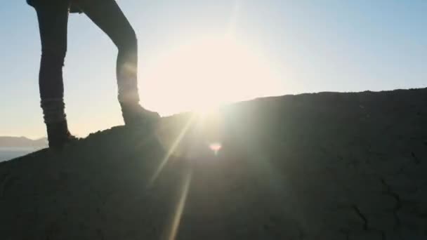 Joven chica atractiva excursionista va a lo largo de las cornisas de arena o acantilado junto al mar. Levanta las manos, mira el dorado amanecer o atardecer. Disfruta de una sensación de éxito. Sube a una montaña alta y hermosa . — Vídeo de stock