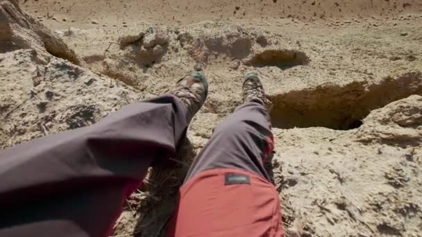 POV: Closeup of hiking boots of an international man. The guy looks at the sea during sunset or sunrise. Hiker goes to the edge of the sandy cliff. Enjoying a vacation trip near the sea — Stock Video