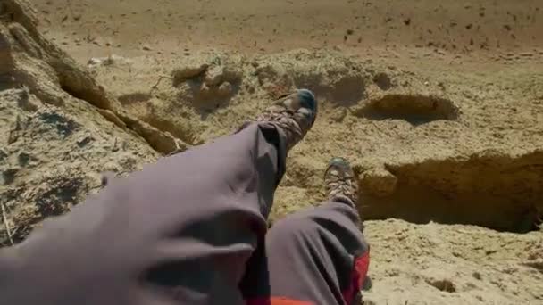 POV: Primer plano de las botas de senderismo de un hombre internacional. El tipo mira al mar al atardecer o al amanecer. El excursionista va al borde del acantilado arenoso. Disfruta de un viaje de vacaciones cerca del mar — Vídeos de Stock