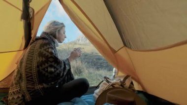 çekici kız Hiking Çadır girişine yakın Dağları arka plan üzerinde oturuyor. Bir kupa kahve veya çay içme. Tatil sahiptir. Dağlarda Özgürlük kavramı. Crimea