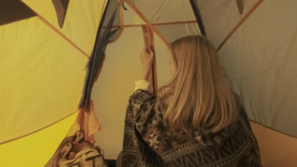 Ung kvinna öppnar tältet entré. Flickan kikar ut ur tältet. Camping i naturen. En resa till landsbygden. En nyfiken turist kikar ur tältet på morgonen. — Stockvideo