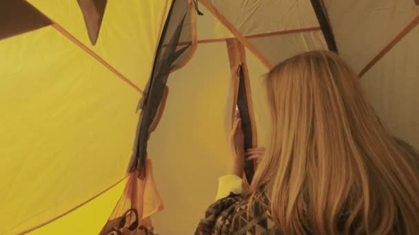 Jonge vrouw opent de ingang van de tent. Het meisje gluurt uit de tent. Kamperen in de natuur. Een reis naar het platteland. Een nieuwsgierige toerist gluurt uit de tent in de ochtend. — Stockvideo