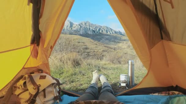 Camping kvinnan ligga i tält nära upp flicka fötter bär Fotvandring stövlar avkopplande semester. Från tält med utsikt över de stora bergen. Vandring livsstil under sommaren. Reser ensam i bergen — Stockvideo