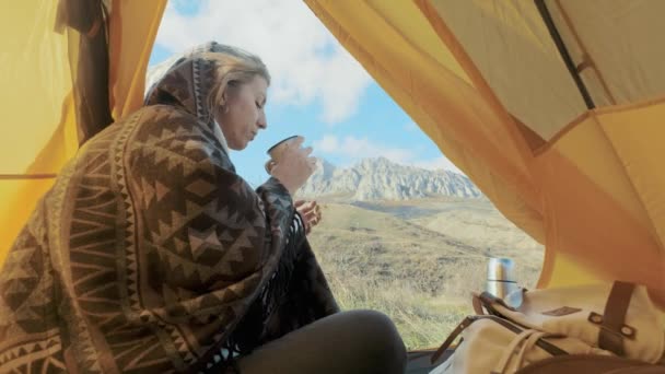 Aantrekkelijk meisje wandelen zit in de buurt van de ingang van de tent op de achtergrond van bergen. Het drinken van koffie of thee uit een mok. Geniet van de vakantie. Het concept van vrijheid in de bergen. Crimea — Stockvideo