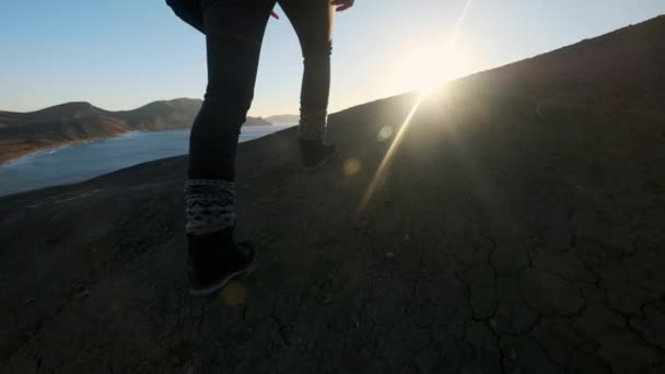 Ung vacker flicka vandrare går längs sandstranden avsatser eller seaside cliff. Höjer händerna upp, ser på gyllene soluppgången eller solnedgången. Har en känsla av framgång. Klättrar på ett högt vackra berg. — Stockvideo
