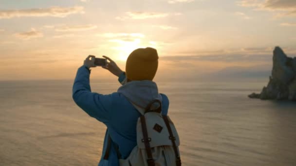 ハイキング魅力的な少女のスマート フォンの写真になります。海沿いの岬に美しい夕日を撮影します。目標に到達。クリミア自治共和国、ウクライナ。自由と自然との調和の概念. — ストック動画