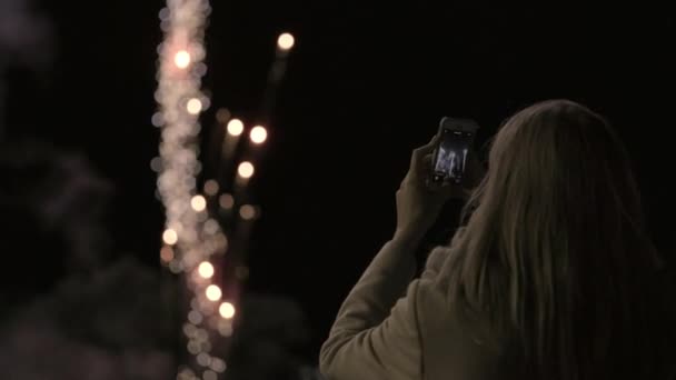 Девушка делает салют на смартфоне. Девушка фотографирует фейерверки на смартфоне. Праздник города, день рождения города . — стоковое видео