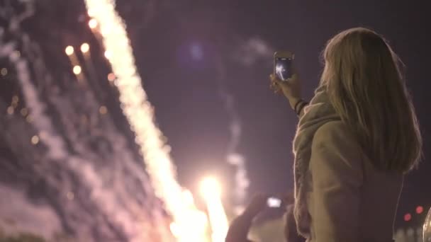 Dziewczyna fotografowania salute na smartfonie. Młoda dziewczyna Zdjęcia fajerwerków na smartfonie. Wakacje w mieście, urodziny miasta. — Wideo stockowe