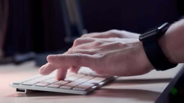 Αρσενικό διαχειριστής δακτυλογράφηση στο πληκτρολόγιο στο γραφείο το βράδυ. Ένα έξυπνο ρολόι είναι φοριέται στο χέρι. Γκρο πλαν. — Αρχείο Βίντεο