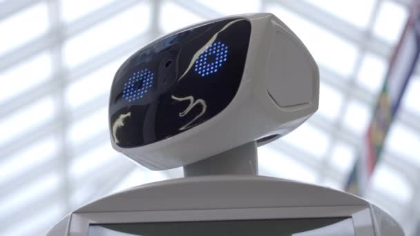 Tecnologías robóticas modernas. El robot mira a la cámara a la persona. Retrato de un robot, gira la cabeza. Robot blanco moderno en la exposición de las nuevas tecnologías . — Vídeos de Stock