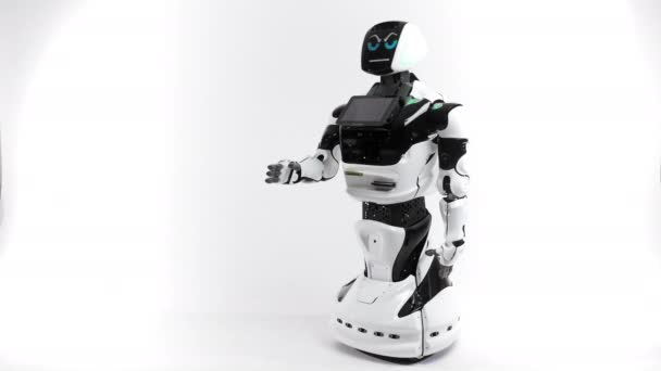 Technologies robotiques modernes. Robot dans le studio lumineux. Android soulève et abaisse la main sur un fond blanc. Montre le mal et les bonnes émotions. Regardant la caméra 