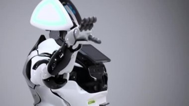 Modern Robotik teknolojiler. Beyaz modern robot parlak bir stüdyoda. Bir tebrik el sallayarak android görüntüleyiciyi selamlıyor. Beyaz zemin üzerinde bir robot gösteri. Burada gelecek.