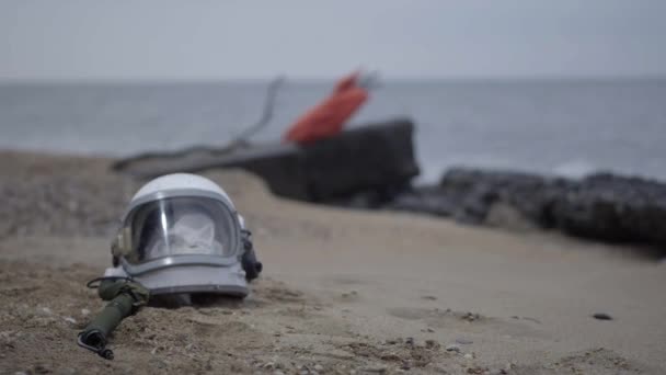Död astronaut på planeten. Skalle från huvudet i hjälmen ligger på sanden vid havet. Besväras av olycka. — Stockvideo