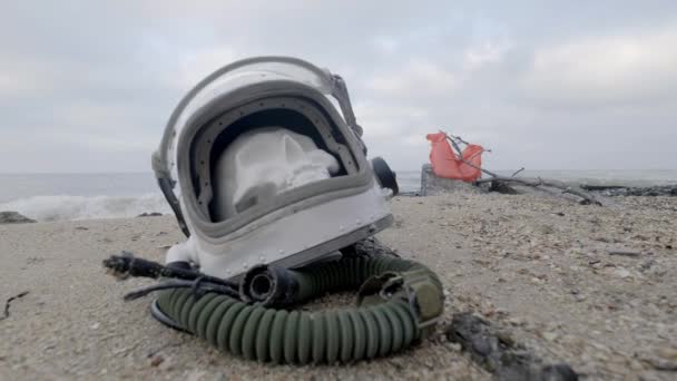 Egy halott űrhajós a fejét a homok, a tenger mellett fekszik. Űrhajós összetört a saját űrhajó. Felhős idő, a szél fúj — Stock videók