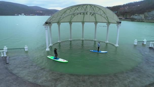 アナパ ロシア - 19.01.2019: 2 人のライダーは、sup サーフボードに浮動小数点値。古い浸水公園の木々 の間で泳ぐ。サーフィンを学ぶ。Sup — ストック動画