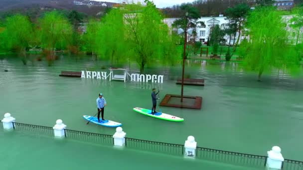 ANAPA RUSSIA - 19.01.2019: Dois pilotos flutuam nas pranchas de surf. Nade entre as árvores no antigo parque inundado. Aprendendo a surfar. SUP — Vídeo de Stock