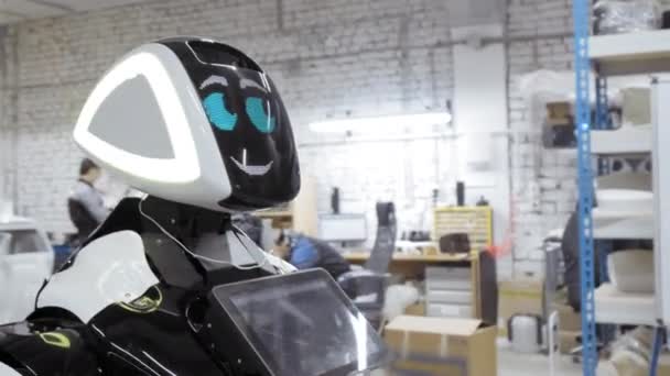 Ein neuer Roboter steht in einem Raum im Dachgeschoss. Anlage zur Produktion von Robotern. Der Roboter blinzelt und lächelt. — Stockvideo