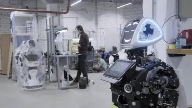 Fabrika Robotlar, modern robot gelişmeler üretimi için. Demonte robot tebrik elinde ve dansları atölye dalgalar. Mühendisler yürüyüş içinde belgili tanımlık geçmiş.