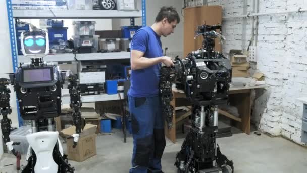 Fábrica para la producción de robots. El ingeniero fija una parte separada de la mano al cuerpo del nuevo robot. Crea un robot . — Vídeos de Stock
