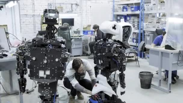 Factory for the production of robots, modern robotic developments. A group of young engineers creates new modern robots. Robots are disassembled in the shop. — Stock Video