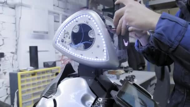 Fábrica para la producción de robots. El científico inserta el tablero - la cara del robot. Da vida al robot . — Vídeos de Stock