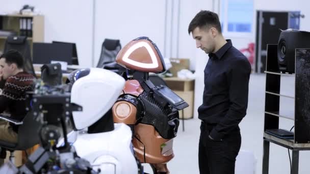 Fábrica para a produção de robôs. O engenheiro ensina o discurso do robô, fala com o robô, ouve as respostas do robô . — Vídeo de Stock