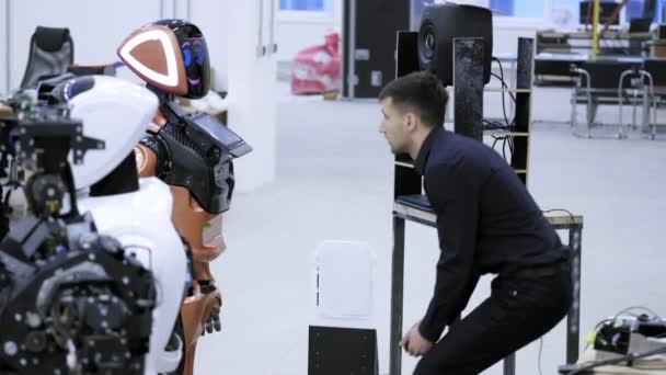 Fábrica para a produção de robôs. O engenheiro ensina o discurso do robô, fala com o robô, ouve as respostas do robô . — Vídeo de Stock