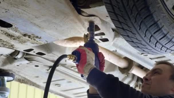 En bil service arbetare skruvar loss bultarna på under sidan av maskinen. Den reparerar bilen, kontrollerar prestandan — Stockvideo