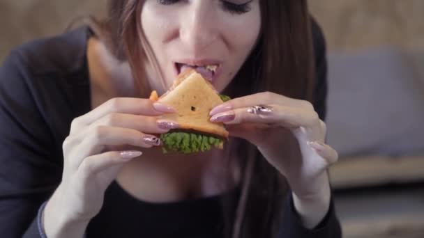 Сексуальная молодая девушка ест седвич. Крупный план. Концепция общества быстрого перекуса и ожирения. Еда для фрилансера — стоковое видео