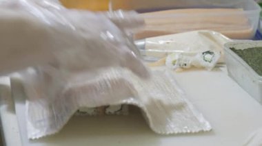 Yakın plan. Suşi pişiren aşçı mutfakta rulo hazırlıyor. Pirinç ve nori büküyor, işi kesiyor. Japonca araçlar kullanıyor.
