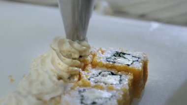 Yakın plan. Suşi pişiren aşçı mutfakta rulo hazırlıyor. Pirinç ve nori büküyor, işi kesiyor. Japonca araçlar kullanıyor.