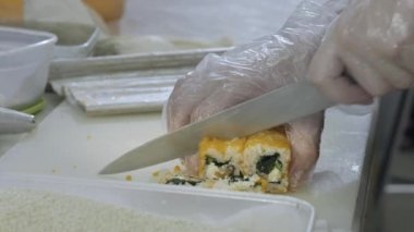Yakın plan. Suşi pişiren aşçı mutfakta rulo hazırlıyor. Pirinç ve nori büküyor, işi kesiyor. Japonca araçlar kullanıyor.