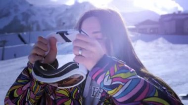 Güzel genç kız kayak gözlükleri giyiyor. Gülümsüyor ve kış tatilinden zevk alır. Kayak veya snowboard için hazır. Snowboard beldesinde kış tatili. Dağın tepesinde yer alan.