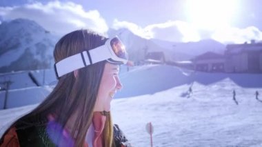Güzel genç kız kayak gözlükleri giyiyor. Gülümsüyor ve kış tatilinden zevk alır. Kayak veya snowboard için hazır. Snowboard beldesinde kış tatili. Dağın tepesinde yer alan.