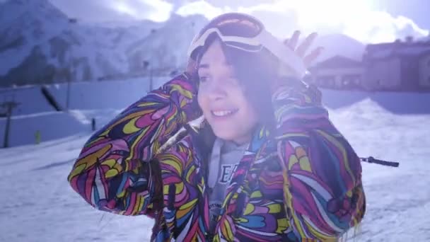 戴着滑雪镜的美丽的年轻女孩。从寒假中微笑和获得快乐。准备滑雪或滑雪板。在滑雪板度假村的寒假。位于山顶. — 图库视频影像