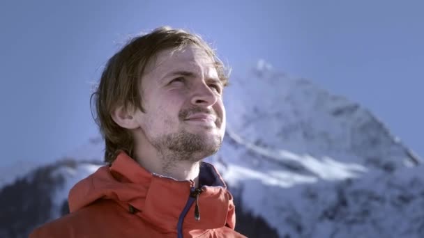 Ένας επαγγελματίας αναβάτης βάζει μια μάλλινη μάσκα του σκι ή μια Μπαλακλάβα στο κεφάλι του. Ετοιμάζομαι για σκι ή σνόουμπορντ. Απολαμβάνει τα χειμερινά αθλήματα. Πίσω από τα μεγάλα χιονισμένα βουνά — Αρχείο Βίντεο