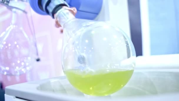 Egy kerek üveglombik forog a laboratóriumban. A laboratóriumi asszisztens lombikban üledéket kap. — Stock videók