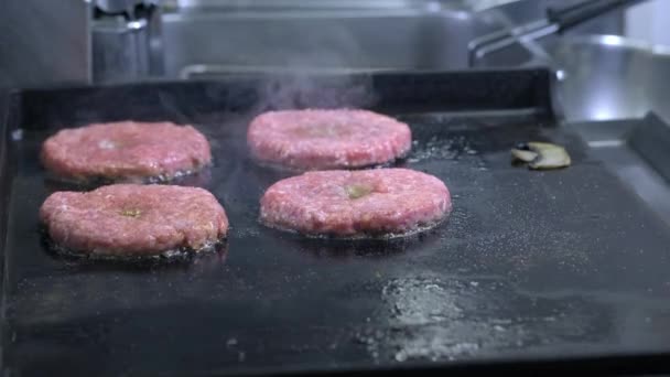 Cozinhar um hambúrguer, hambúrguer ou bife. Em um fogão quente, um cozinheiro frita a carne em uma cozinha profissional. O cozinheiro verifica a prontidão da carne e vira o pedaço de carne. Quadro macro — Vídeo de Stock