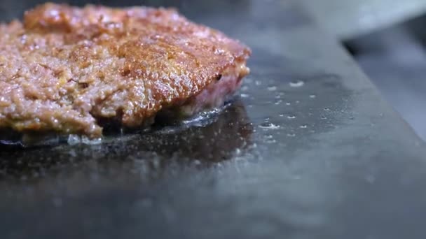 Cuire un hamburger, une galette ou un steak. Sur une cuisinière chaude, un cuisinier fait frire la viande dans une cuisine professionnelle. Le cuisinier vérifie l'état de préparation de la viande et retourne le morceau de viande. Cadre macro — Video