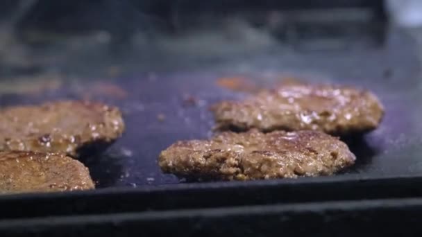 Cozinhar um hambúrguer, hambúrguer ou bife. Em um fogão quente, um cozinheiro frita a carne em uma cozinha profissional. O cozinheiro verifica a prontidão da carne e vira o pedaço de carne. Quadro macro — Vídeo de Stock