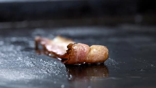 Gros plan de tranches de bacon grillées sur un gril chaud. Un cuisinier dans une cuisine professionnelle frites et tourne tranches de bacon — Video