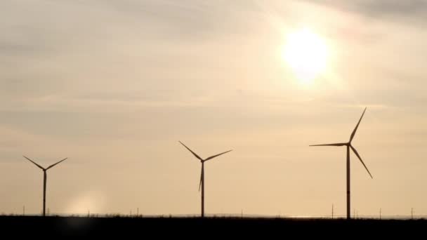 Evening silhouette of windmills with sun setting in background on a cloudy blue sky. These clean energy generating wind farms are densely populated in the state — Stock Video