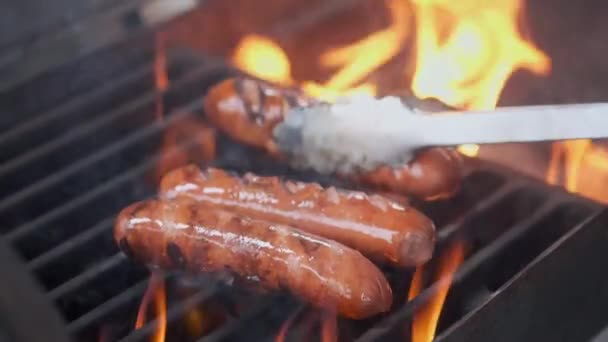 Sabrosas salchichas jugosas a la parrilla sobre un fuego. Cocinero preparando salchichas en la parrilla. Tira la parrilla y da la vuelta. Vacaciones familiares de verano . — Vídeo de stock