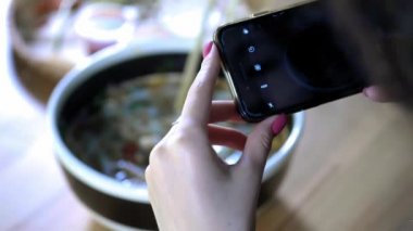 Bir kız akıllı telefonda yiyecek bir fotoğraf yapar. Arkadaşlarınızla sosyal ağlarda gıda bir fotoğraf ile paylaşın. Asya yemekleri ile Cafe. Sosyal aktif yaşam tarzı, arkadaşlarınızla sanal iletişim.
